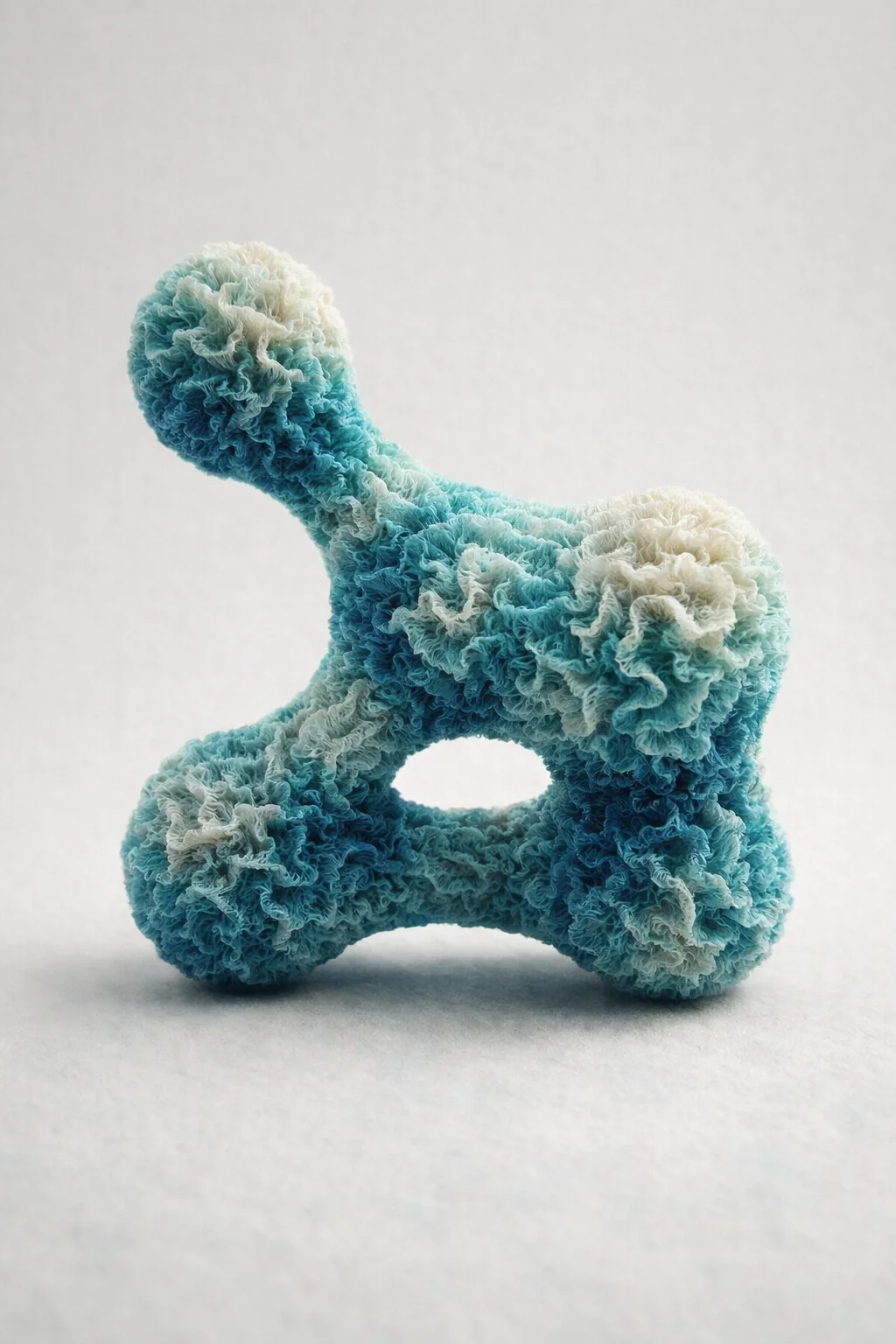A fluffy, coral-like object of fused spheres in blue and white on a light grey ground